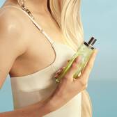 New Starlicious Pistachio Praline in hand asset featuring a model with long blonde hair and blue eyes, wearing a pale yellow dress holding the pistachio praline fragrance bottle