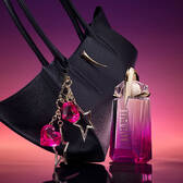 Mugler Alien Pulp bottle standing beside a sleek black handbag adorned with a sparkling pink star and heart charm