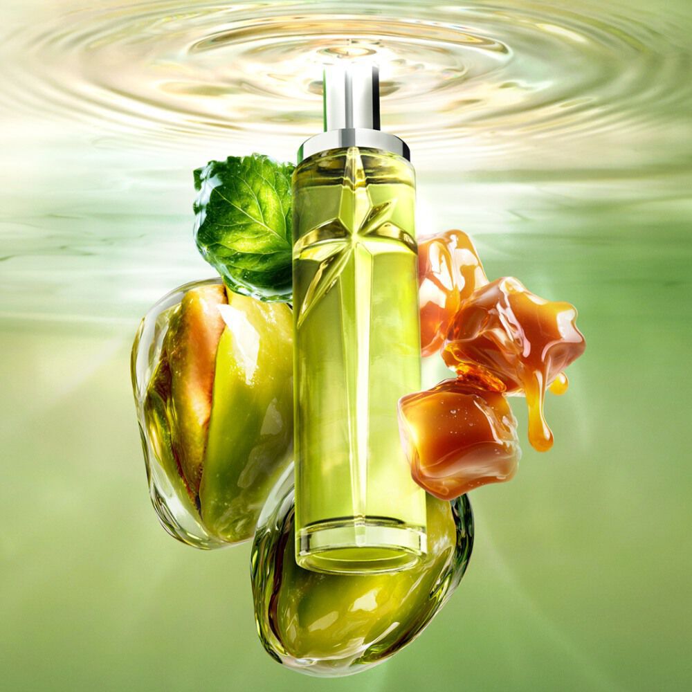 New Starlicious Pistachio Praline still life image featuring the slender bottle surrounded by its key ingredients: a patchouli leaf, whole pistachios, and dripping caramel cubes, all set against a luminous green rippling water background.