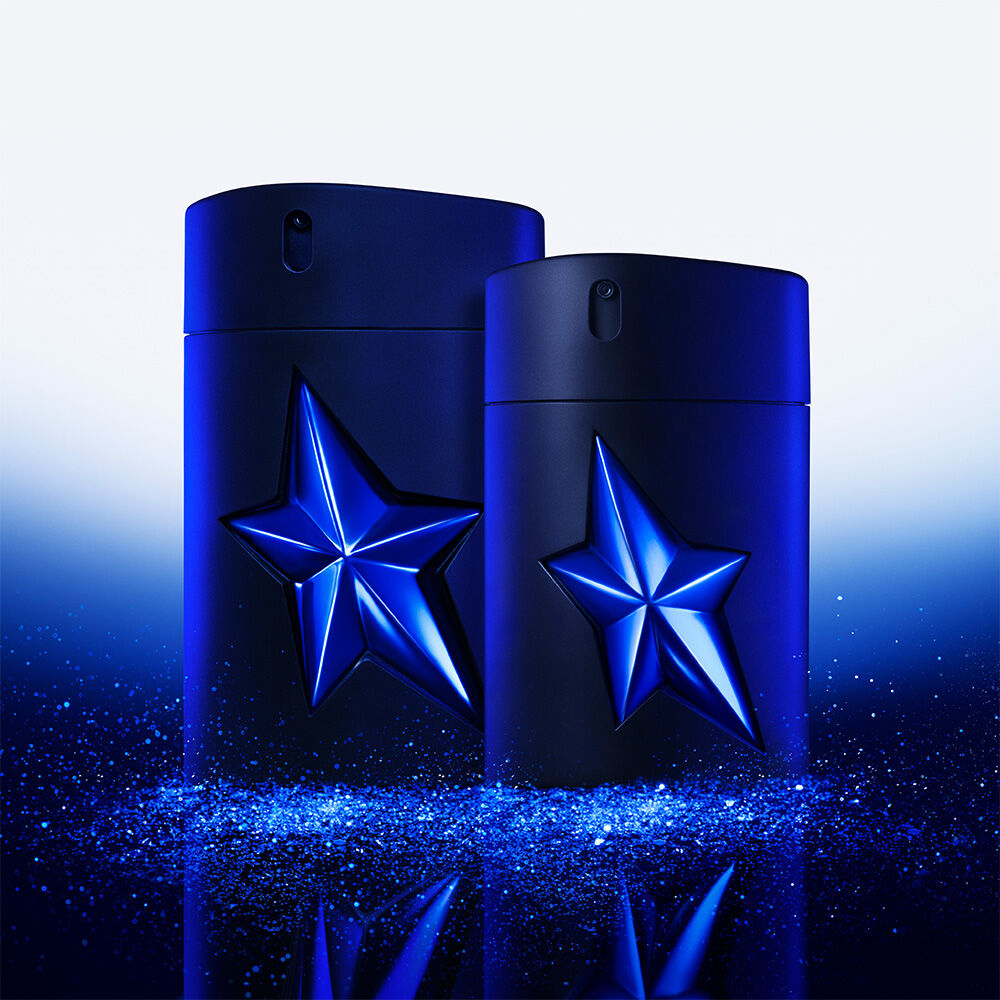 Two A*Men Stellar Eau de Parfum bottles, one 100ml and one 50ml, both dark blue with luminous blue stars, stand side by side on a reflective surface covered in sparkling blue glitter.