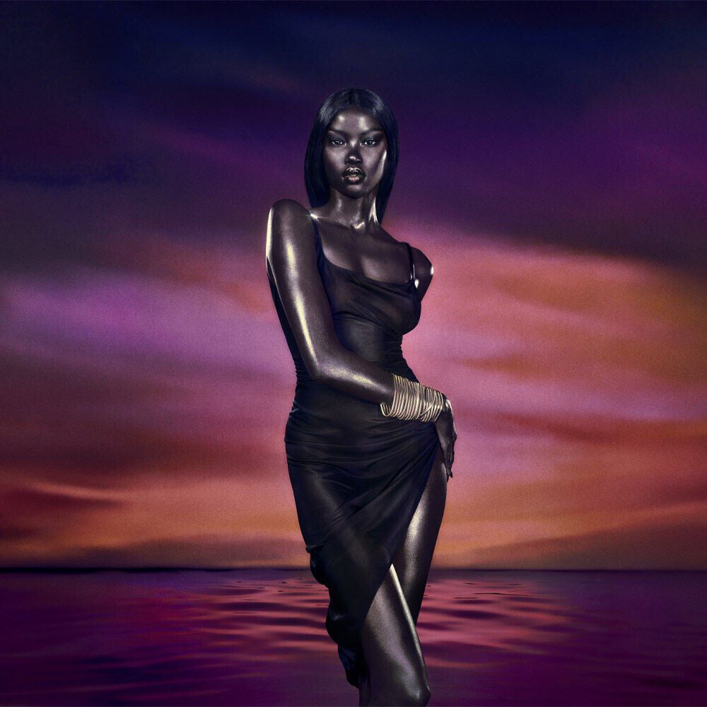  Stylized image of a woman in a dark, draped garment, standing gracefully against a dramatic purple and orange sunset over water
