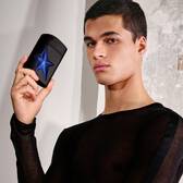 An A*Men Stellar Eau de Parfum bottle is centrally placed on a textured, sparkling blue surface that reflects light.