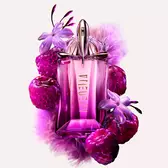 Mugler Alien Pulp bottle amidst juicy pink berries, delicate purple flowers, and soft lavender feathers