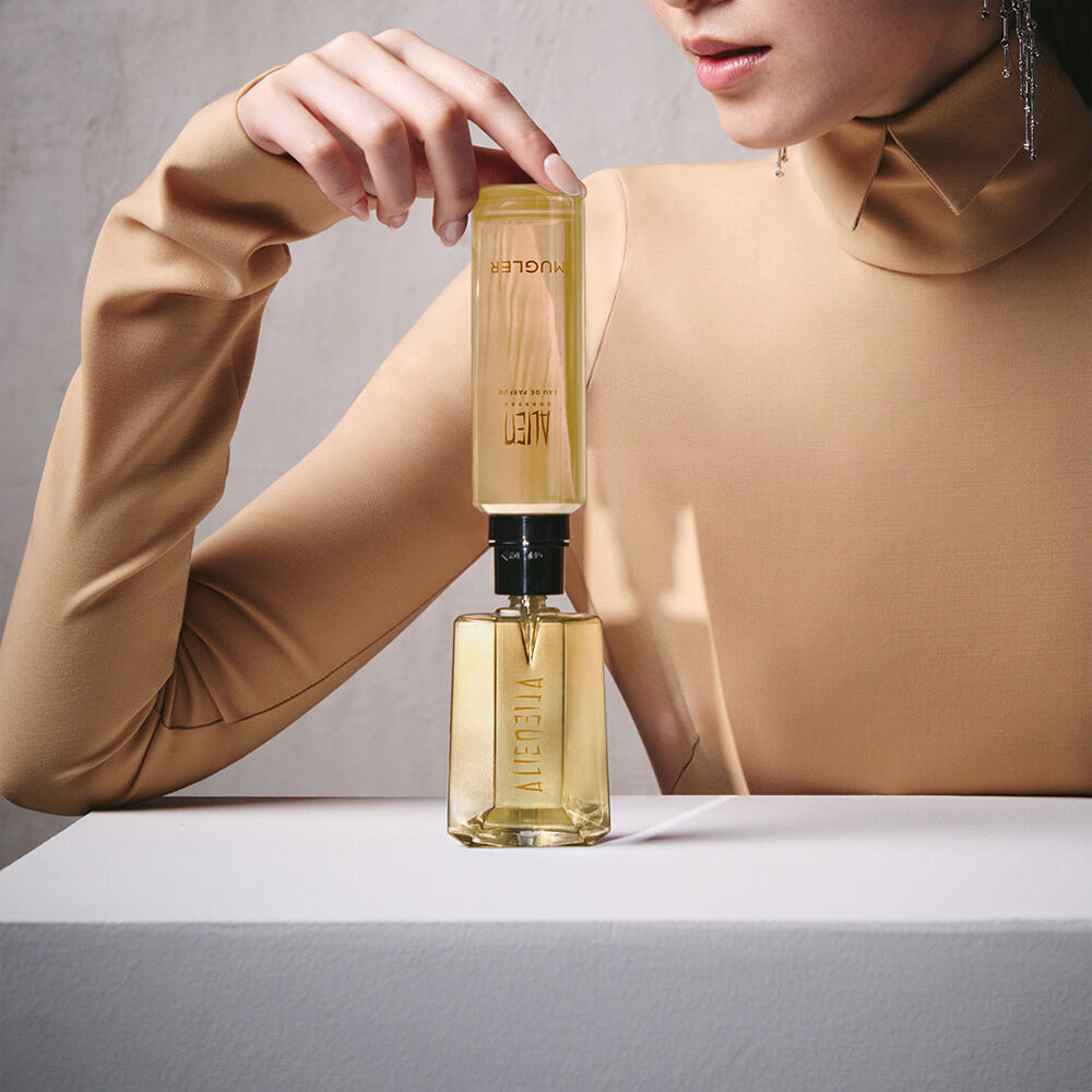 Model refilling an Alien Goddess perfume bottle with a matching refill bottle