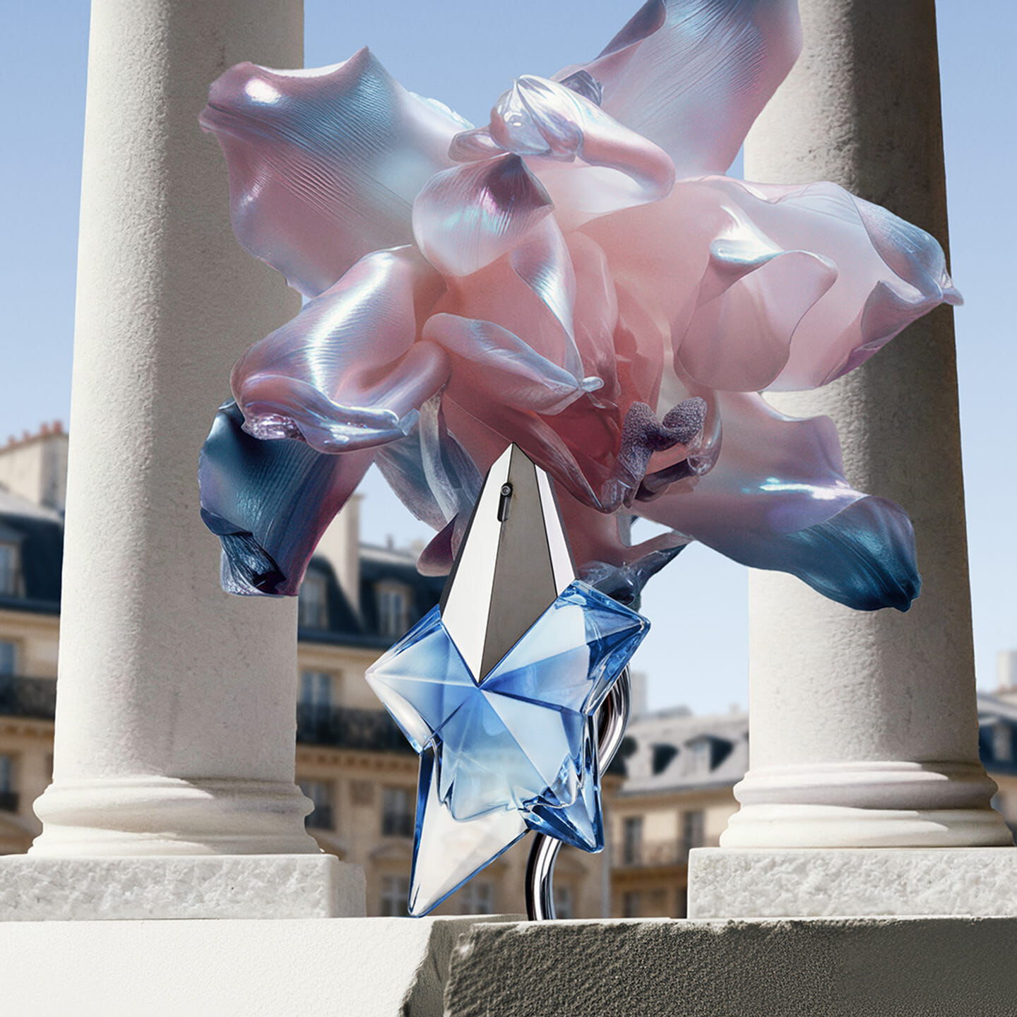 The iconic Angel blue star bottle positioned on a Parisian stone ledge between classical pillars, framed by ethereal iridescent fabric flowers.