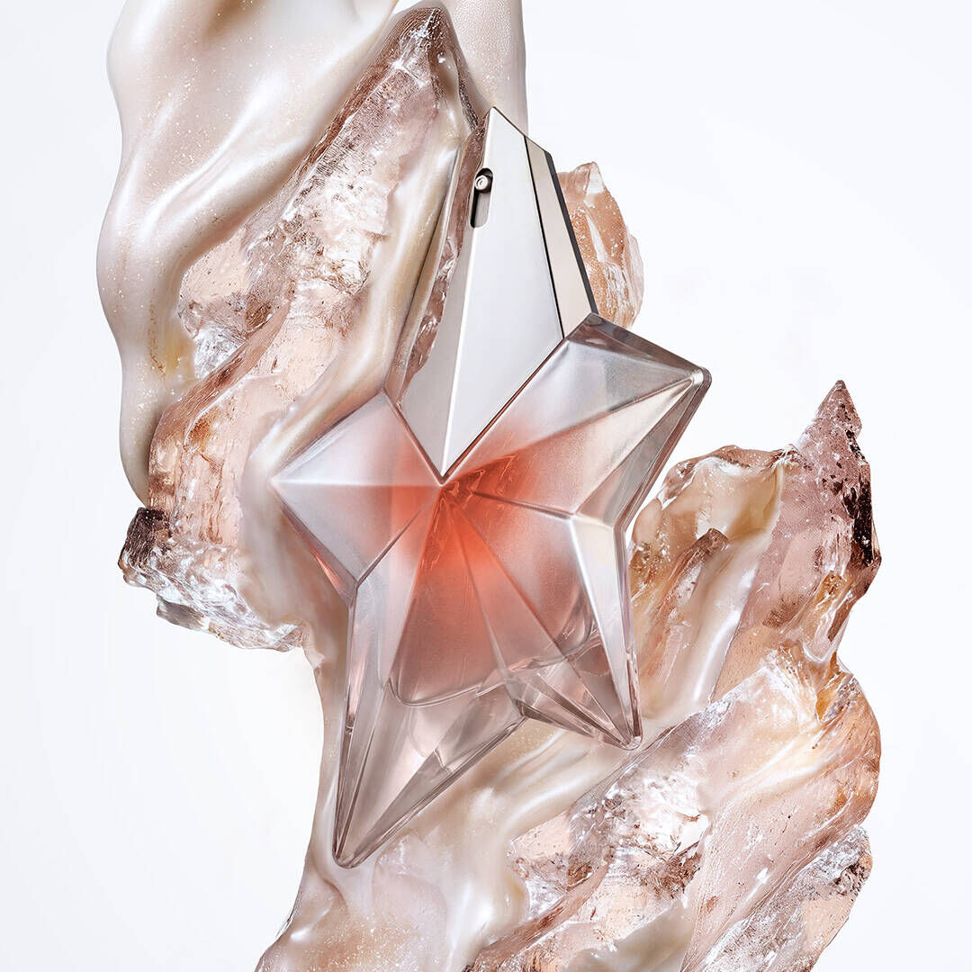 The Angel Blush star bottle surrounded by creamy almond milk swirls, textured sandalwood, and radiant musks, illustrating the fragrance's key olfactory notes.