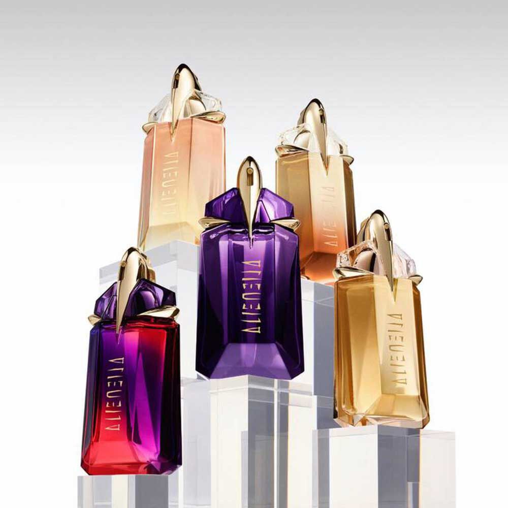 Five Mugler Alien perfume bottles in different shades displayed on clear pedestals
