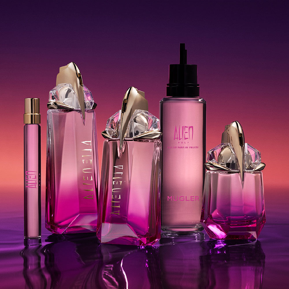 A collection of Mugler Alien Pulp fragrance bottles and body spray on a reflective purple surface, showcasing the full product line in various sizes.
