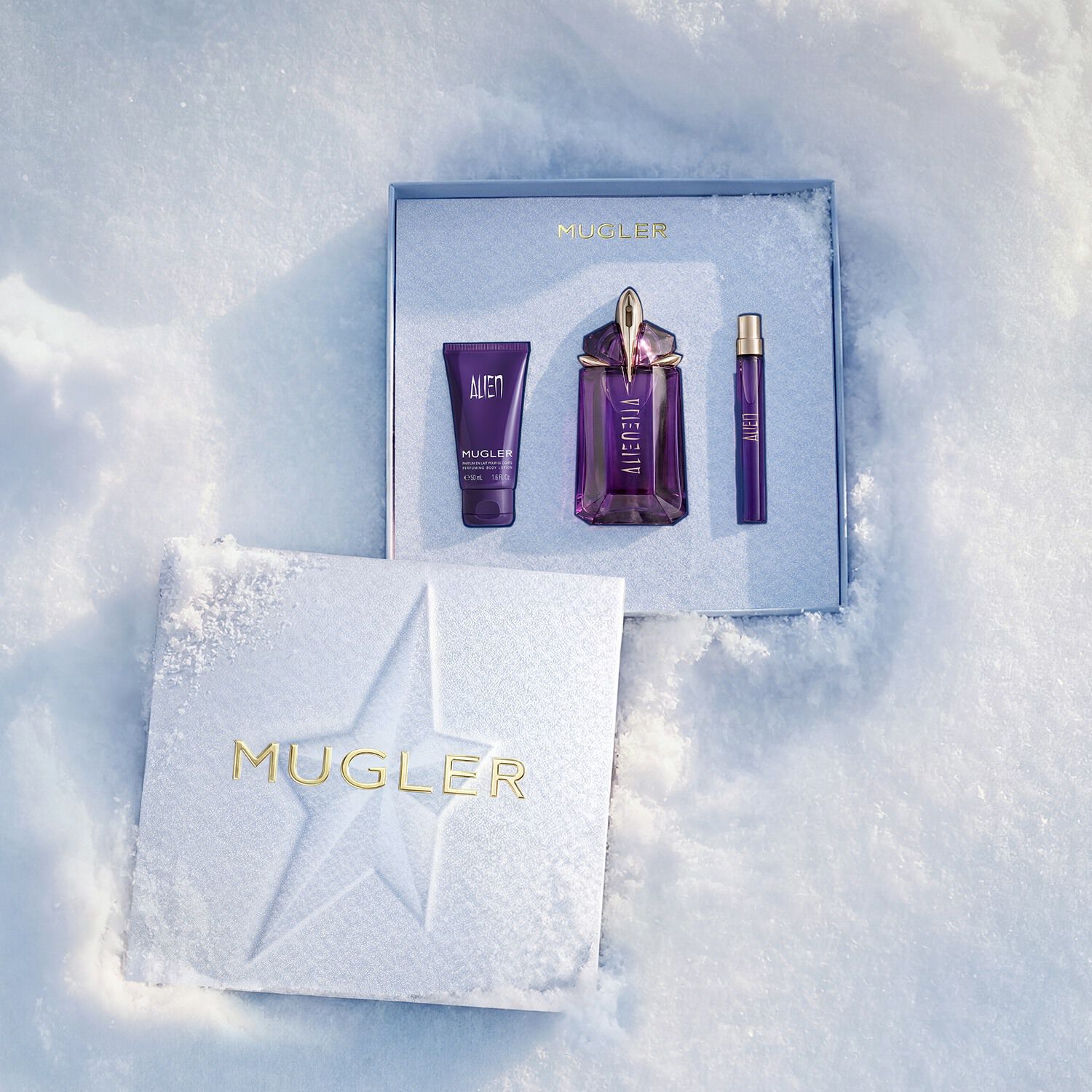 An open, textured ice-blue glistening Mugler gift set resting on snow, revealing an alien eau de parfum 60ml gift set