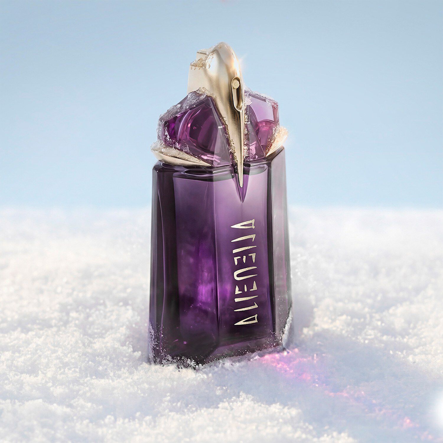 The signature deep purple, talisman-like Mugler Alien eau de parfum perfume bottle standing upright in a soft drift of white snow under bright, clean light.