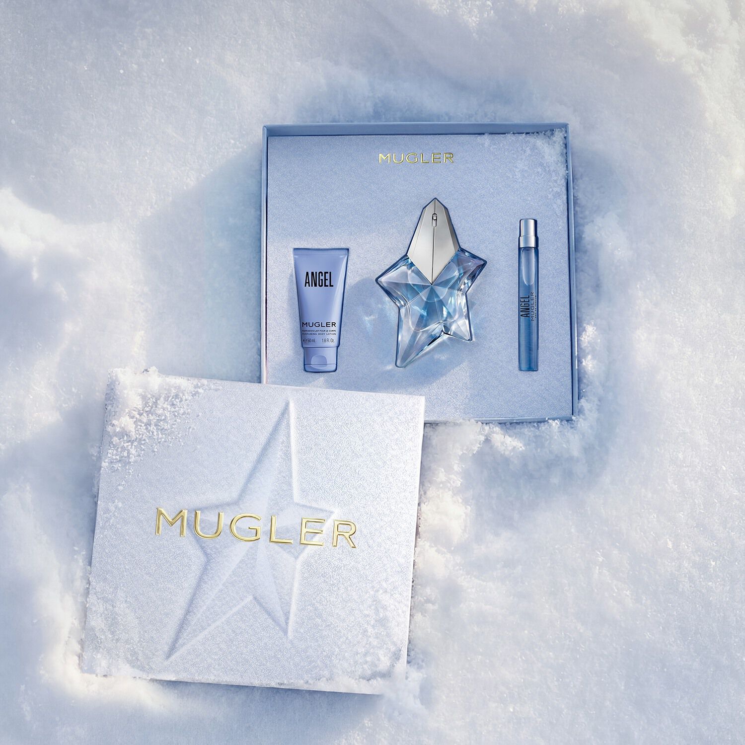 An open, textured ice-blue glistening Mugler gift set resting on snow, revealing an angel eau de parfum 50ml gift set
