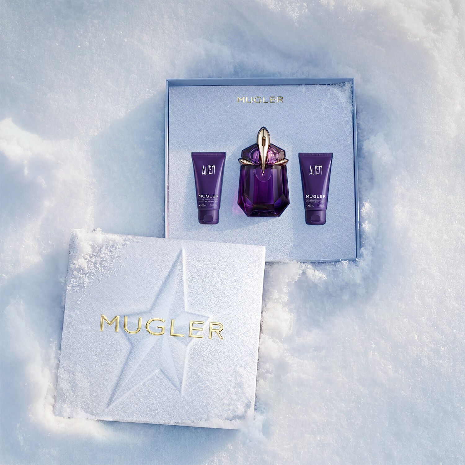 An open, textured ice-blue glistening Mugler gift set resting on snow, revealing an alien eau de parfum 30ml gift set