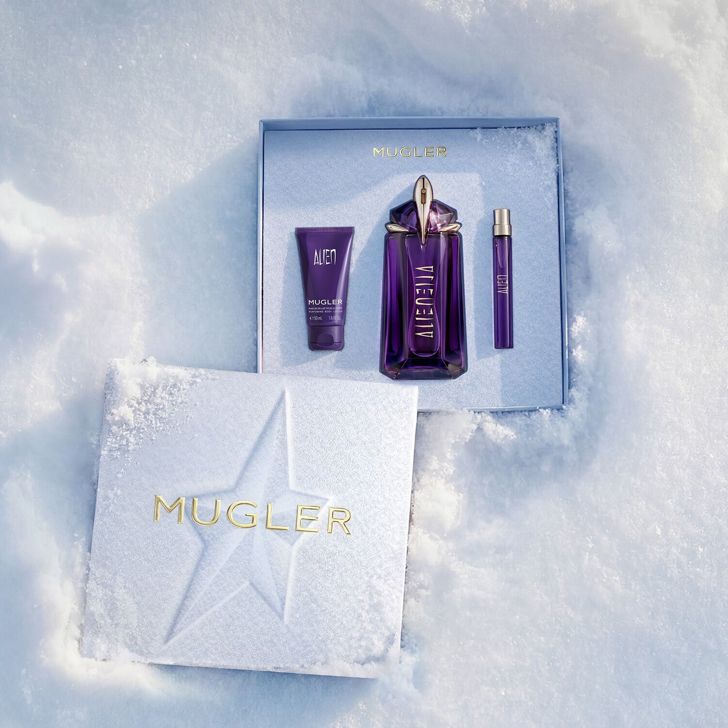 An open, textured ice-blue glistening Mugler gift set resting on snow, revealing an alien eau de parfum 90ml gift se