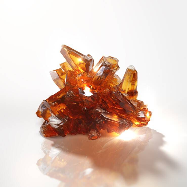A cluster of sparkling amber crystals arranged in a jagged formation, illuminated from below to enhance their transparency and shine.