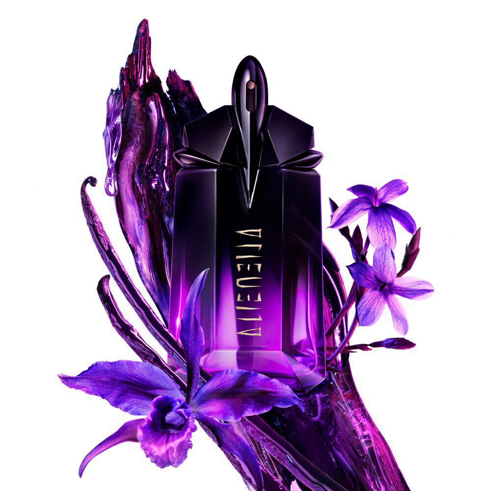 A purple and black Alien perfume bottle, adorned with vibrant purple orchids, delicate purple flowers, and dark, textured vanilla bean pods, set against a pristine white background.