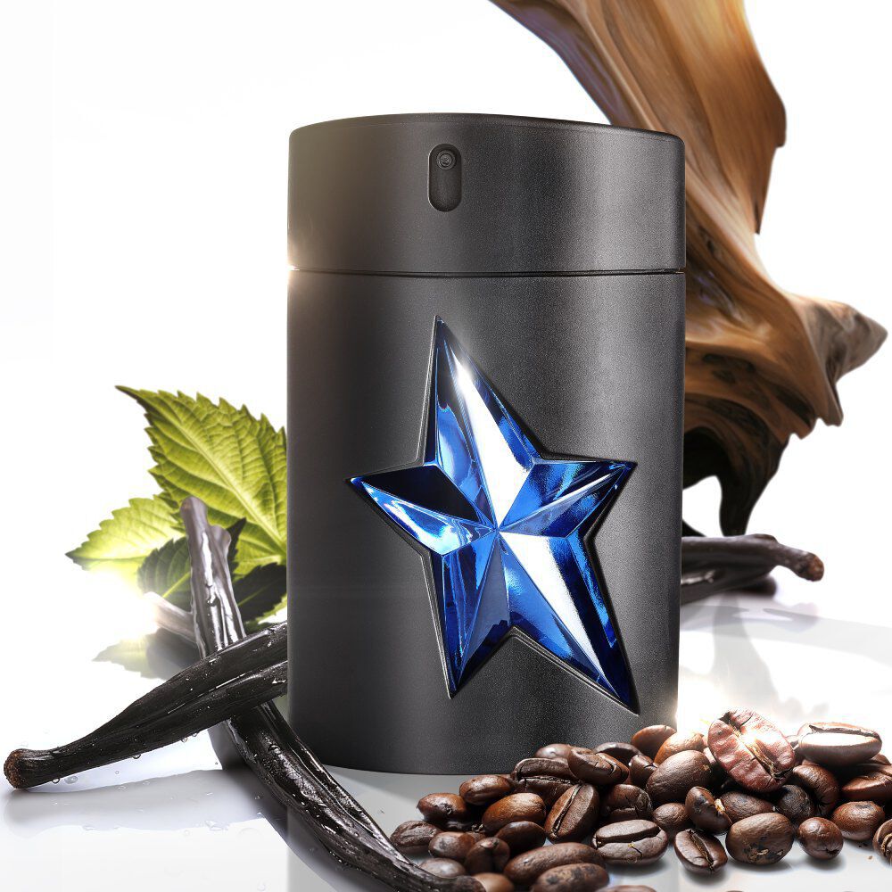 A matte black perfume bottle with a gleaming blue star, surrounded by vanilla pods, coffee beans, a green leaf, and a piece of gnarled wood, against a white background.