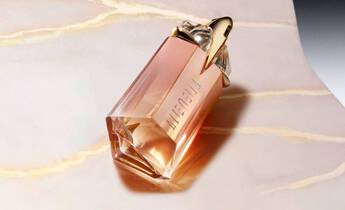 A stylish glass perfume bottle with a rose-gold hue sits elegantly on a smooth, light-colored surface, featuring unique geometric design and a decorative cap.