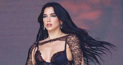 A woman with long black hair wearing a lace top and earrings, posing confidently against a colorful background.
