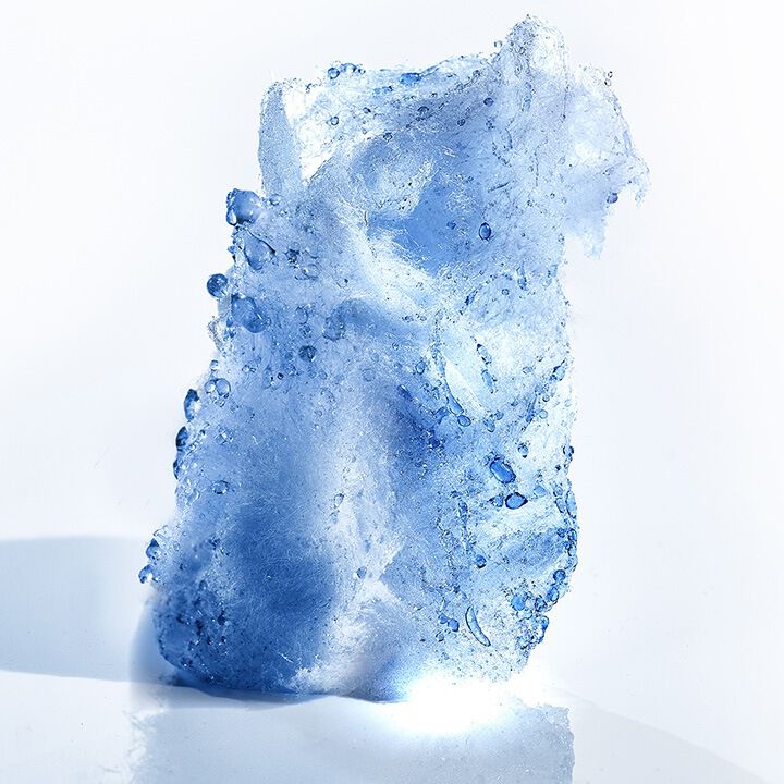 A translucent blue ice sculpture with bubbles and a textured surface, illuminated against a white background.