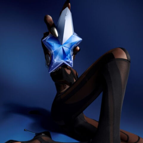 A stylized figure wearing black clothing holds a blue star-shaped object against a dark blue background, exuding an air of elegance and mystique.
