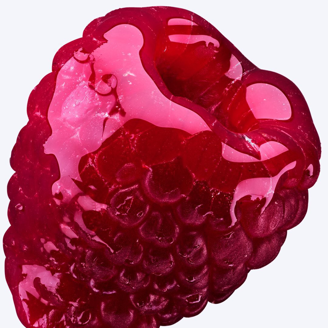 A close-up image of a glossy, translucent raspberry, featuring water droplets on its surface, illuminated from below. The vibrant red color and the shiny texture create a striking visual effect.