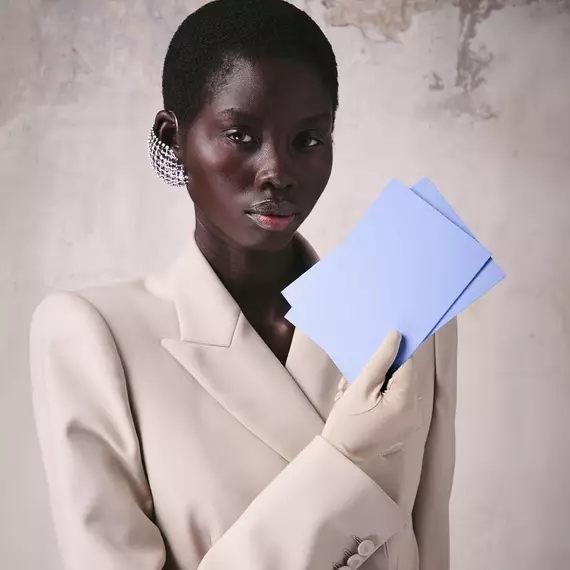 Model in beige blazer holding two light purple Mugler cards.