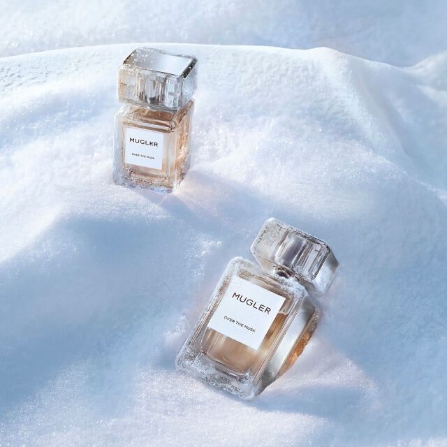 two Mugler Les Exceptions elegant, heavy-glass rectangualr Mugler perfume bottles filled with golden liquid, sitting at angles in a snowy landscape. the text reads "luxury gifts"