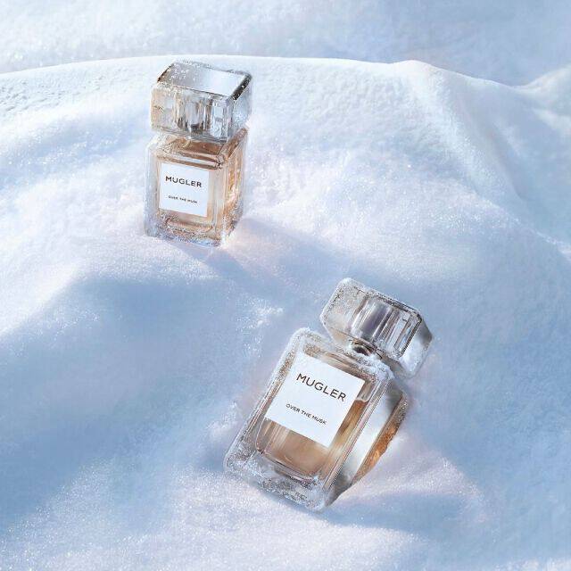 two Mugler Les Exceptions elegant, heavy-glass rectangualr Mugler perfume bottles filled with golden liquid, sitting at angles in a snowy landscape. the text reads "luxury gifts"