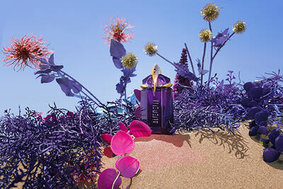 A vibrant purple perfume bottle surrounded by colorful flowers and lush foliage against a bright blue sky.