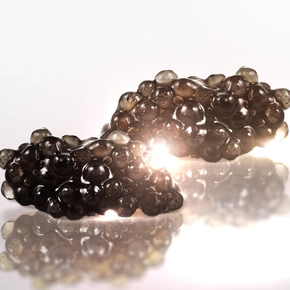 Two clusters of shiny, dark, bubble-like formations are displayed on a reflective surface, creating an artistic and abstract appearance with soft lighting enhancing their texture.