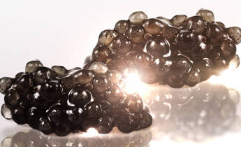 Two clusters of shiny, dark, bubble-like formations are displayed on a reflective surface, creating an artistic and abstract appearance with soft lighting enhancing their texture.