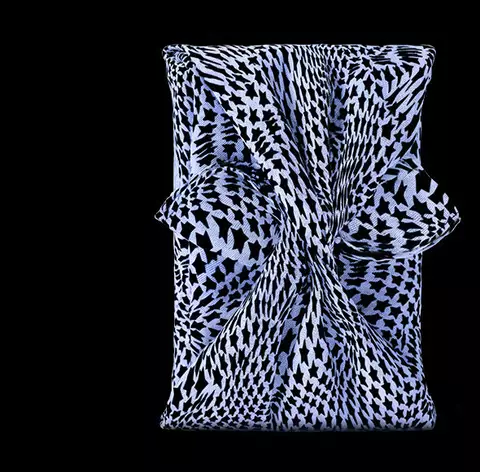A stylized blue star-shaped perfume bottle next to an elegantly patterned fabric pouch against a black background.