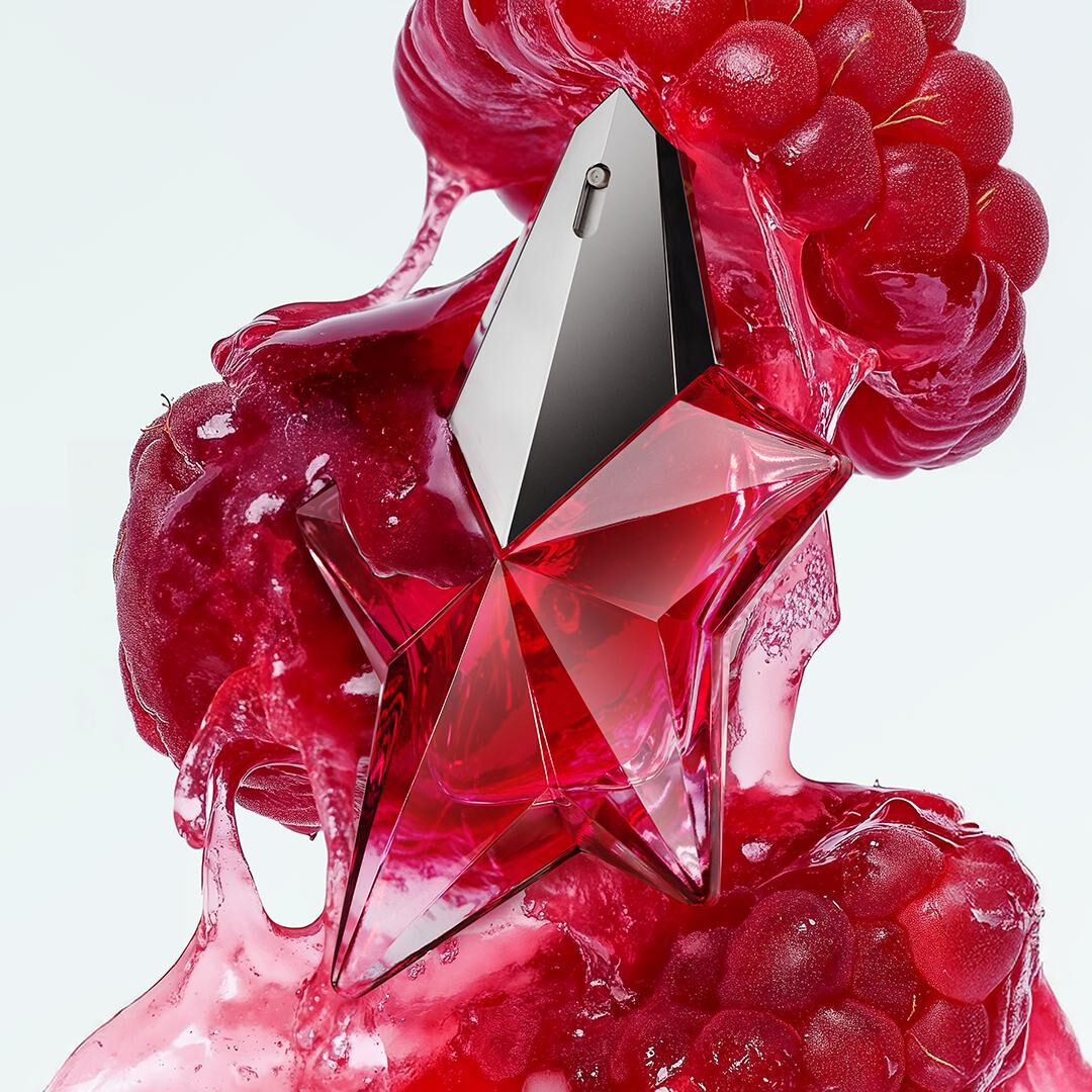 Captivating red star-shaped perfume bottle surrounded by luscious red fruit pulp, suggesting a daring fruity floral woody fragrance.