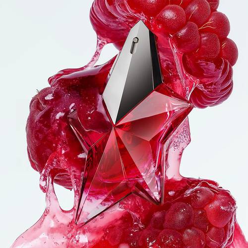Captivating red star-shaped perfume bottle surrounded by luscious red fruit pulp, suggesting a daring fruity floral woody fragrance.