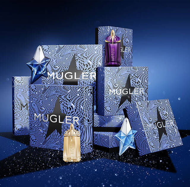 A collection of Mugler perfume bottles and elegantly designed gift boxes arranged in a dynamic display against a deep blue background, with sparkling details adding a festive touch.