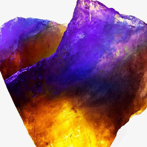 A large, multifaceted crystal displaying a vibrant gradient of purple, orange, and yellow hues.