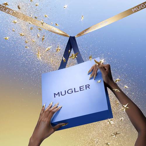 Two hands with long, golden metallic nails hold a blue Mugler shopping bag. A gold ribbon
            with the Mugler logo is tied around the bag's handles, and golden stars and glitter fall around it.