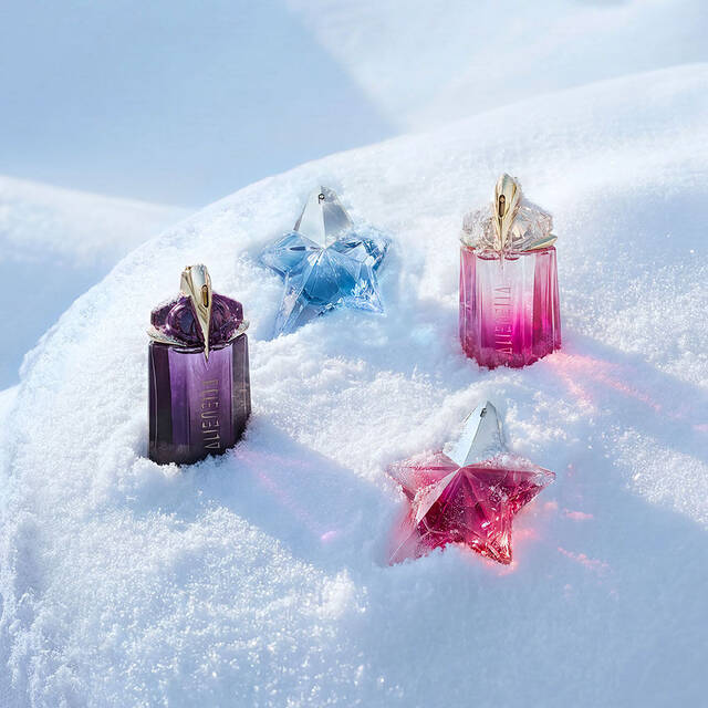 A purple Mugler Alien bottle, a light blue Angel bottle, a pink Alien bottle, and a pink Angel bottle beautifully spaced out on a soft, undulating snow surface. image redirects to our gift guide