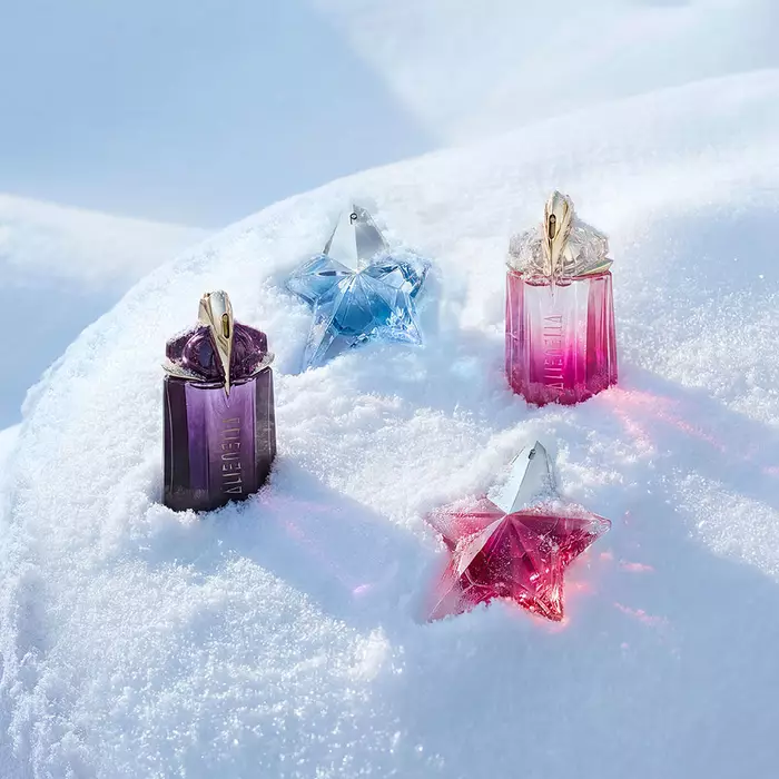 A purple Mugler Alien bottle, a light blue Angel bottle, a pink Alien bottle, and a pink Angel bottle beautifully spaced out on a soft, undulating snow surface. image redirects to our gift guide