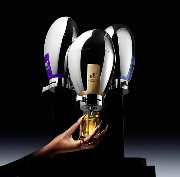 A hand reaches for a golden liquid from a sleek, modern display featuring three elegantly designed bottles set against a dark background.