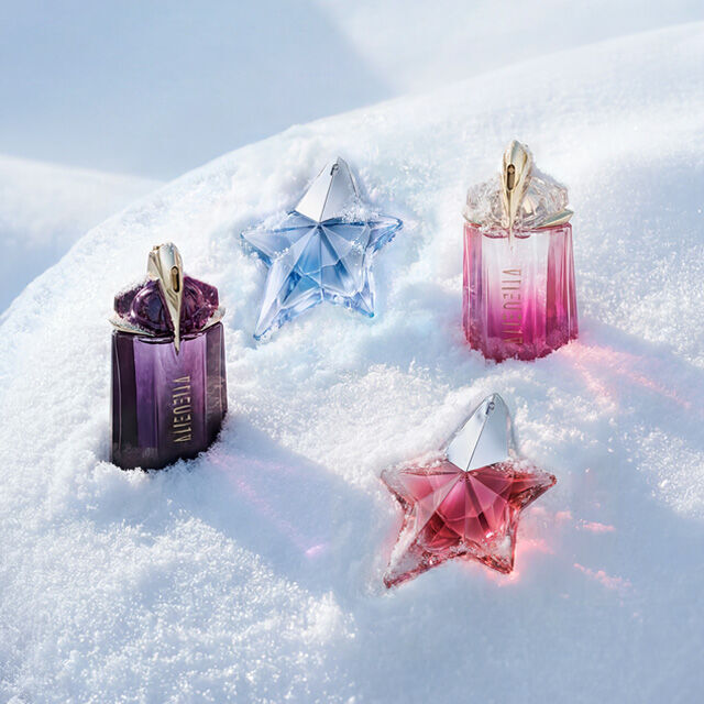 A purple Mugler Alien bottle, a light blue Angel bottle, a pink Alien bottle, and a pink Angel bottle beautifully spaced out on a soft, undulating snow surface. text reads "the frozen hour is here. enter a frosted landscape and discover gifts that leave an impression. frosted treasures for your loved ones, or yourself, that capture a glistening opulence. shop before the ice melts"