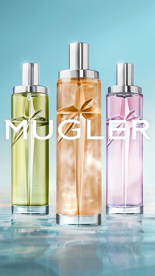 Three slender, tall Mugler Starlicious perfume bottles with silver caps and embossed signature stars, standing on a reflective water surface. The juices – green, shimmering orange, and soft pink – glow against an ethereal blue-to-cream gradient