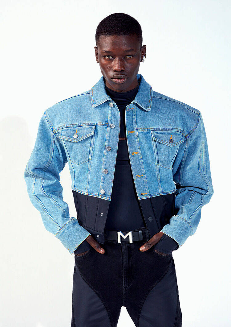 A model poses confidently in a cropped denim jacket over a fitted black top, showcasing a modern and stylish look.