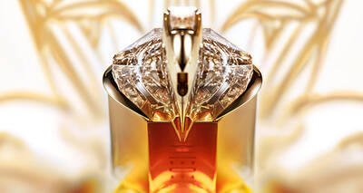 A close-up of an elegant perfume bottle with a luxurious design, featuring a faceted crystal cap and a warm amber liquid inside, against a soft, blurred background.