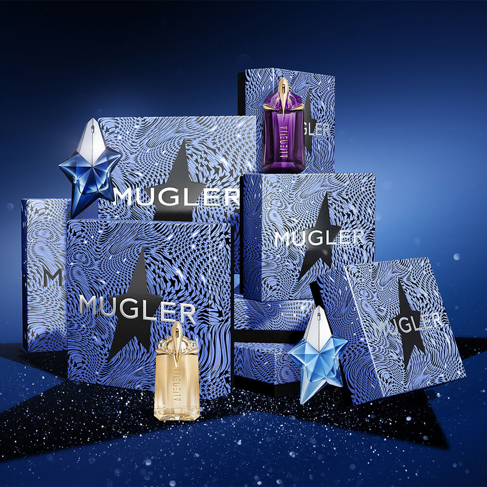 A collection of beautifully packaged Mugler perfume bottles arranged on a dark star-shaped display, set against a deep blue background with sparkles.