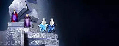 An array of Mugler fragrances, including Alien and star-shaped Angel bottles, displayed on branded gift boxes against a dark background.