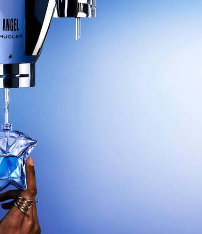 A hand reaching to catch a blue star-shaped perfume bottle as liquid is dispensed from a sleek silver perfume dispenser against a gradient blue background.