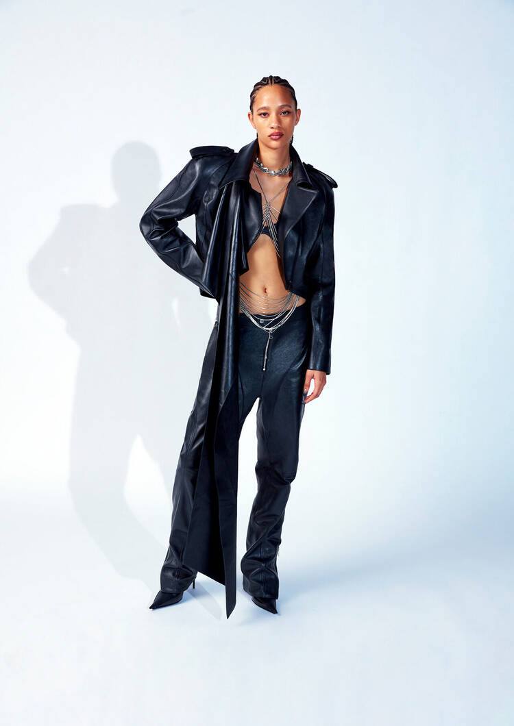 A model poses confidently in edgy black leather attire, featuring a cropped jacket and form-fitting pants, complemented by layered silver jewelry.