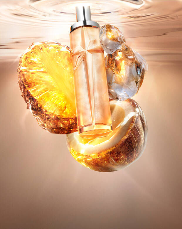 New Starlicious Pineapple Musk still life featuring the slender glass bottle surrounded by its key ingredients: a glowing pineapple slice, a cracked coconut shell, and crystalline musk, all set against a warm, luminous rippling water background.