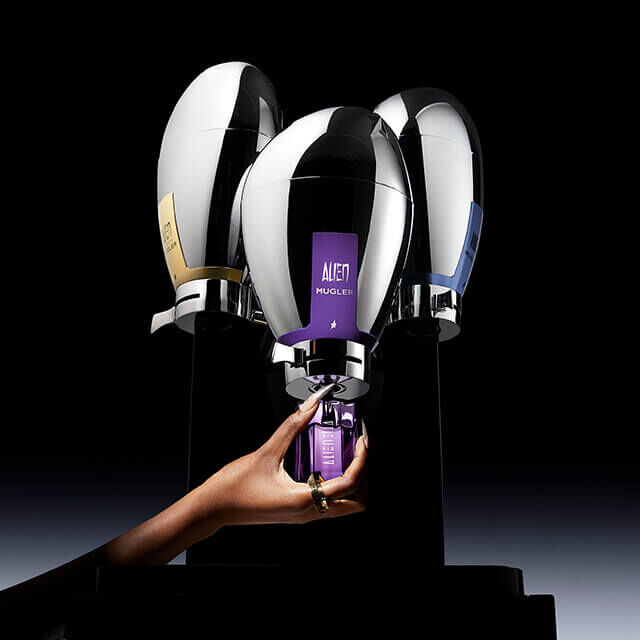 A hand reaching for a sleek, modern bottle of skincare product, surrounded by three shiny, stylized containers on a dark background.